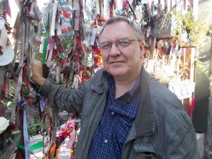 A man with short grey hair and glasses standing next to a lot of ribbons.