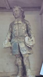 Damaged statue of a boy holding a book. Almost all the paint is gone.