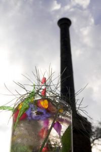 The top of a cocktail decorated with flowers and greenery, with the chimney of the engine house in the background.