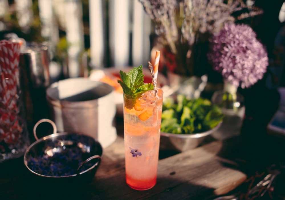 A cocktail in a tall glass, with flowers, leaves, and a red and white striped paper straw in it.