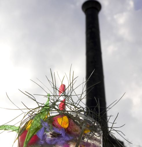 The chimney of the Engine House of the Brunel Museum in the background (slightly out of focus) with the top of a cocktail in focus in the foreground with pretty flowers in the glass.