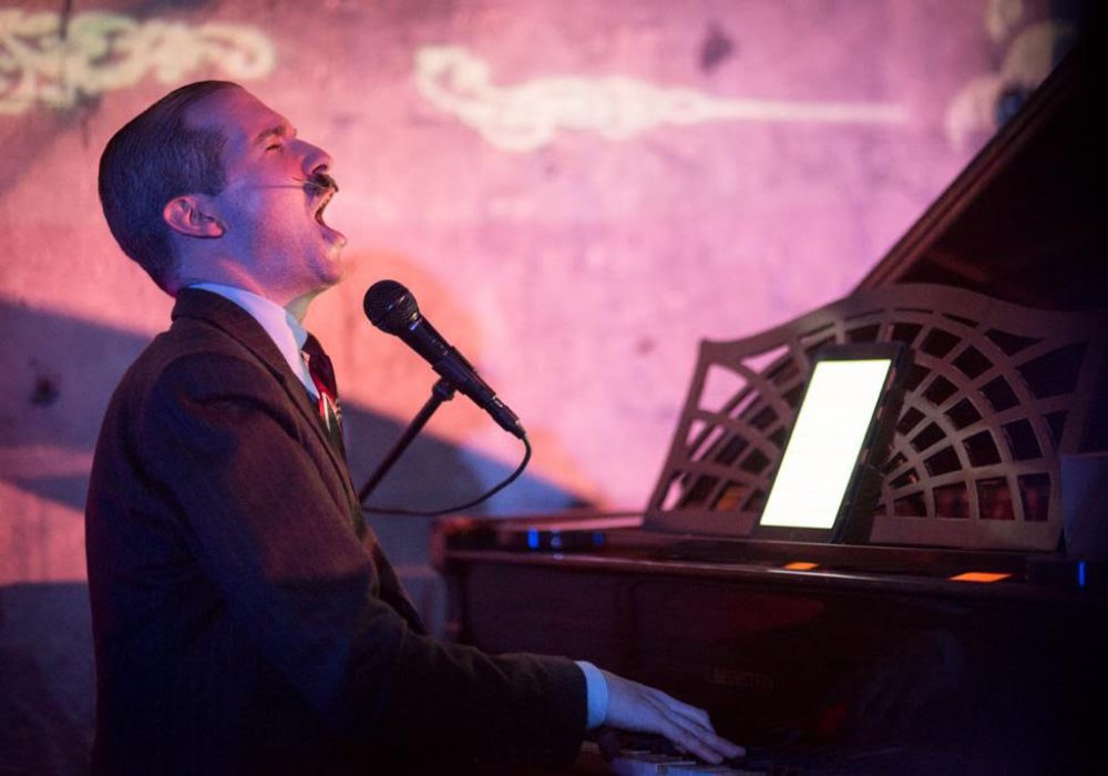 Man with moustache singing at a piano