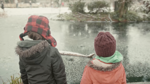 Two children face a river. Film still from My Extinction Film.