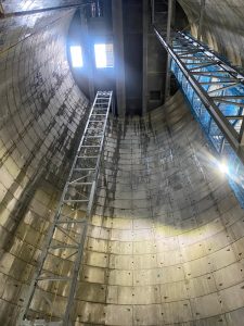 The camera looks up through a long cylindrical tunnel shaft is lined with concrete blocks. Two metal scaffolds stand at each side of the shaft. 